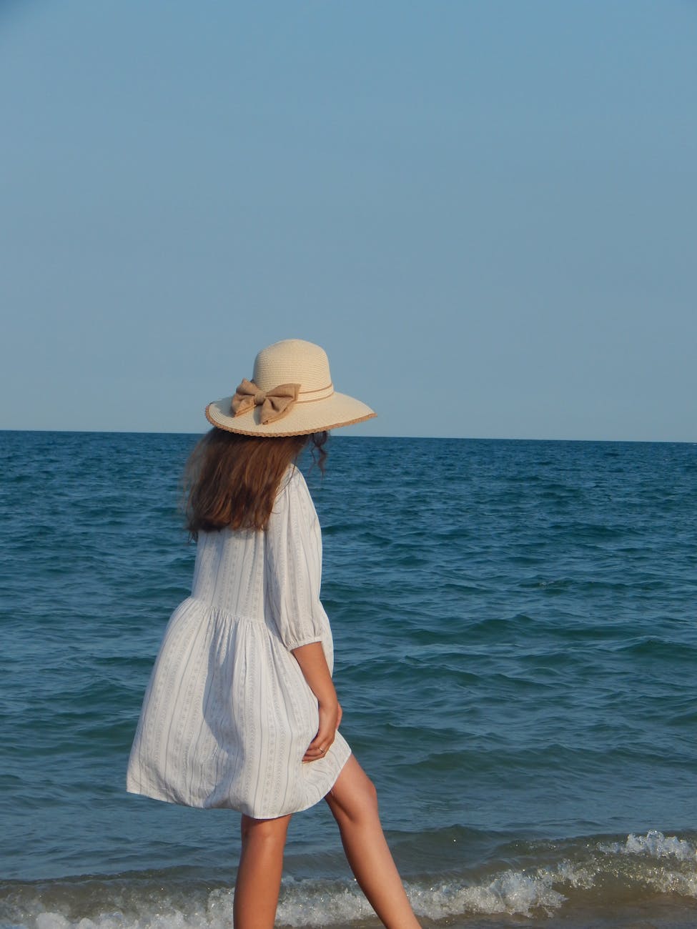 woman in a white dress and hat walking on a shore